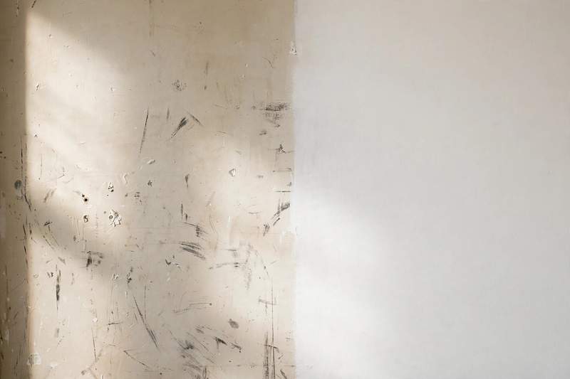 Close-up photo of an apartment wall showing minor scuff marks and small nail holes next to a freshly painted clean section
