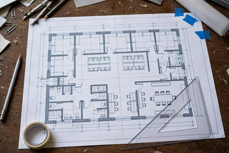 Architectural floor plan blueprint with measurement lines and a scale ruler on a desk for office space planning