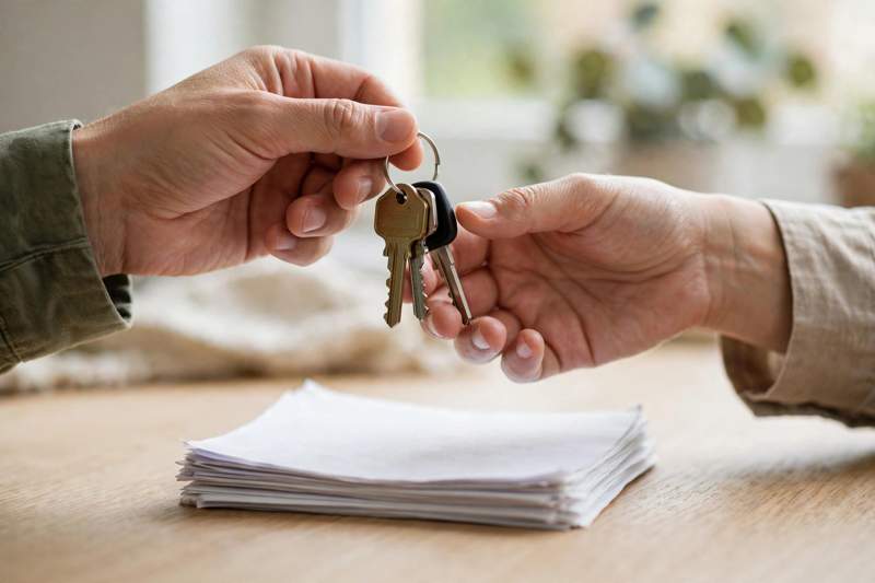 Two hands exchanging a set of house keys over paperwork, illustrating a security deposit return